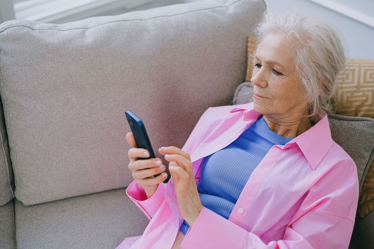Frau um die 70 schreibt auf dem Sofa eine Nachricht