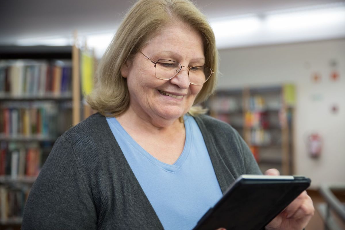 Frau um die 70 lernt in der Bibliothek das Tablet kennen