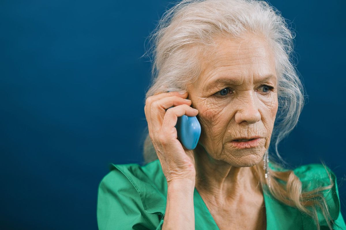 Frau mit grauen Haaren am Telefon, sie hört skeptisch zu