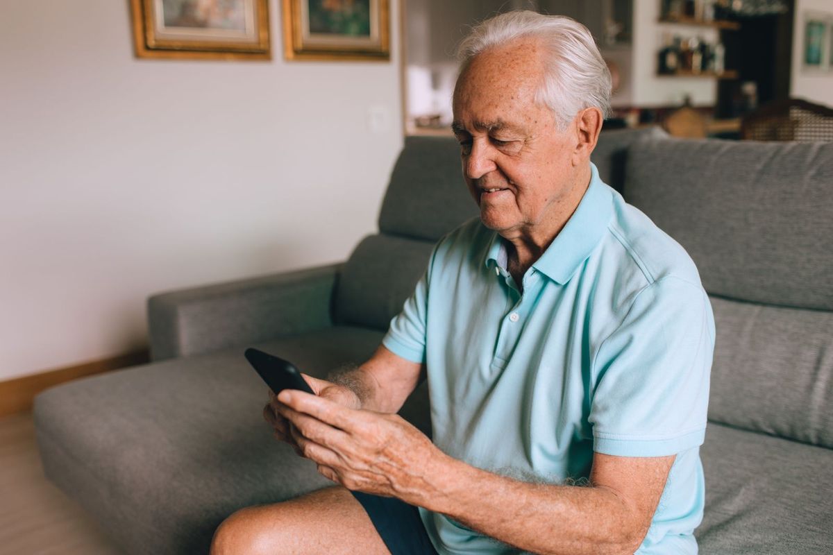 Mann um die 65 liest auf dem Sofa eine Nachricht auf dem Smartphone