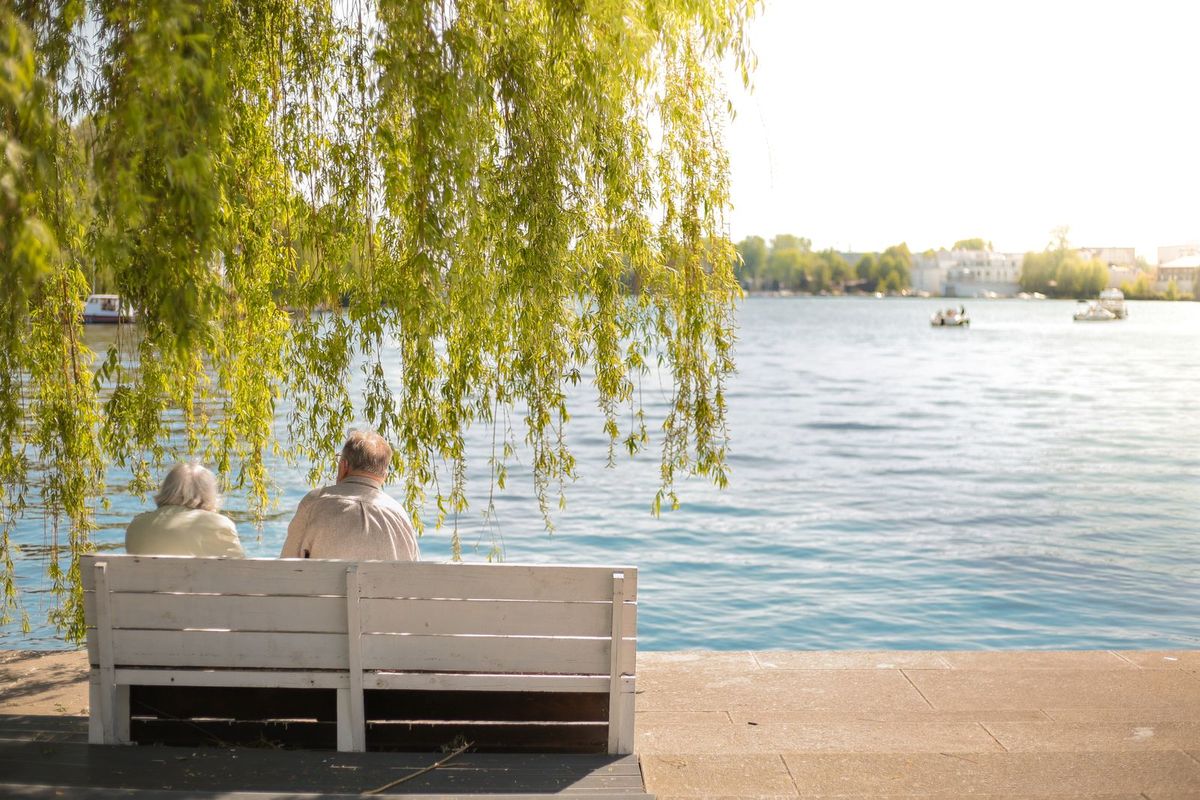 Paar sitzt auf einer Bank unter einer Weide am See